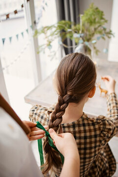 A woman braids a girl's braid and ties it with a bow 