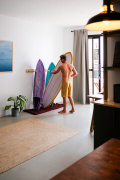 A young man wearing a bermuda shorts arranging his surfboards
