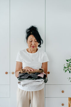 Senior asian woman standing near closet, reasonable consumption