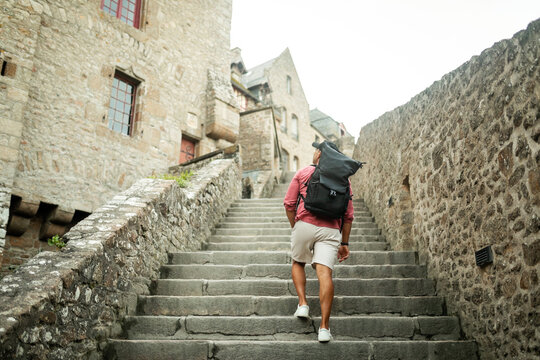tourist man walking through mont saint michel with his backpack