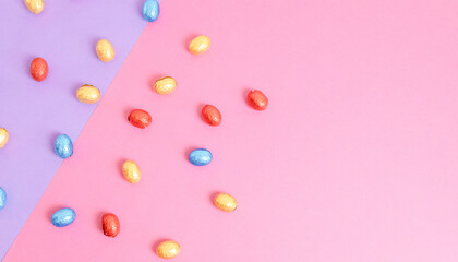 Chocolate Easter eggs in a colorful wrapper on a lilac-pink background.