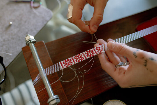 a woman weaves a bracelet from beads