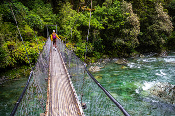 hiker crossing a rushing river in fiordland national park, new zealand south island, hiking trail to lake marian