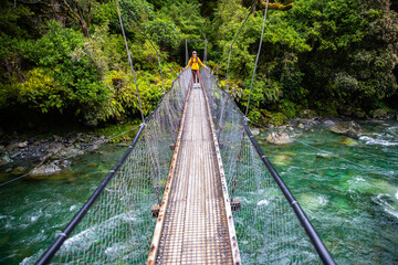 Fototapeta premium hiker crossing a rushing river in fiordland national park, new zealand south island, hiking trail to lake marian