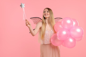 Beautiful girl in fairy costume with wings, magic wand and balloons on pink background