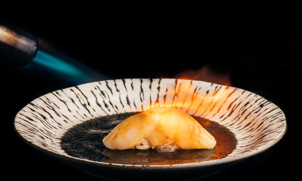 Scallop nigiri heated with blowtorch on plate on dark backdrop