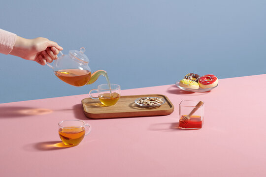 Woman pouring hot tea from teapot into glass on table