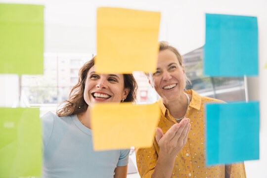 Businesswomen Putting Post-It Notes On Glass Board