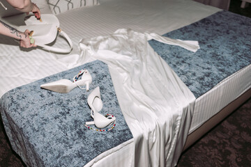 Cozy bed with wedding dress and high heels in hotel bedroom