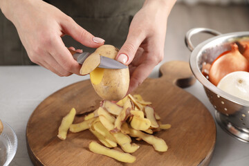 Woman peeling fresh potato with knife at light table indoors, closeup