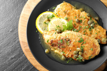 Delicious chicken piccata on black table, top view