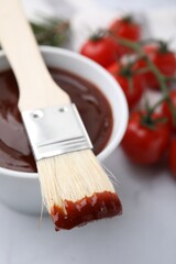 Marinade in bowl and basting brush on white table, closeup