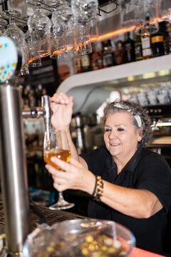 Senior woman pouring beer in glass.