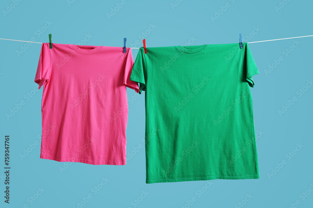 Sticker Colorful t-shirts drying on washing line against light blue background