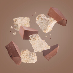 Pieces of tasty halva and chocolate falling on brown background