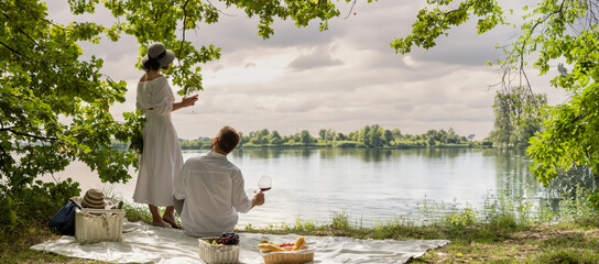 happy married couple spends time on a picnic. a man and a woman relax together, enjoy nature, drink wine, spend the weekend together.