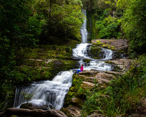 Obraz premium lovely hiker girl sits and admires mighty McLean Falls surrounded by stunning native rainforest in Catlins Forest Park, Otago, New Zealand, hidden gems of NZ south island