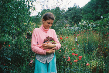 Young woman with armful of grapes in summer garden