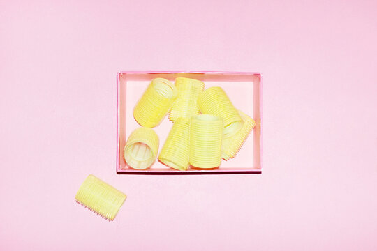Neon yellow hair curlers on a pink background with hard flashlight