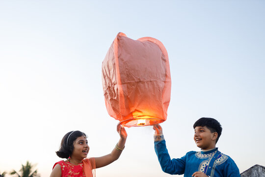 Happy brother and sister releasing sky lantern at twilight