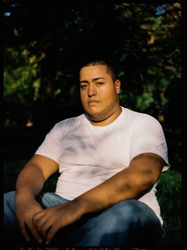Black Plus-Size guy sitting on the grass looking into the camera.