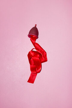 Conceptual photo of period / menstrual cup & red silk ribbon as blood