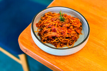 Spaghetti with tomato sauce on a plate on a wooden table ready to be served in a Thai restaurant.