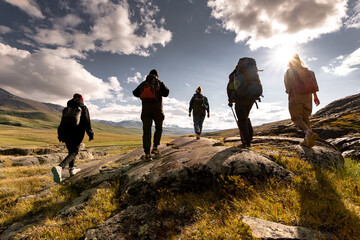 Group of tourist silhouettes with backpacks walks in sunset mountains
