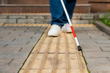 A blind woman walks outdoors using a cane along a tactile yellow tile.