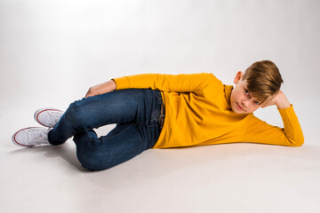 Cute young boy in a yellow hoodie lying on the floor with his head propped up with one hand
