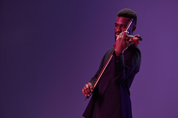Elegant man in black suit playing violin on purple background creating a harmonious music scene