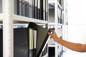 Hand of businessman office worker searching files and paperwork in the archive or document archiving storage room shelf for folder binder finding or data report record or workplace photo concept.