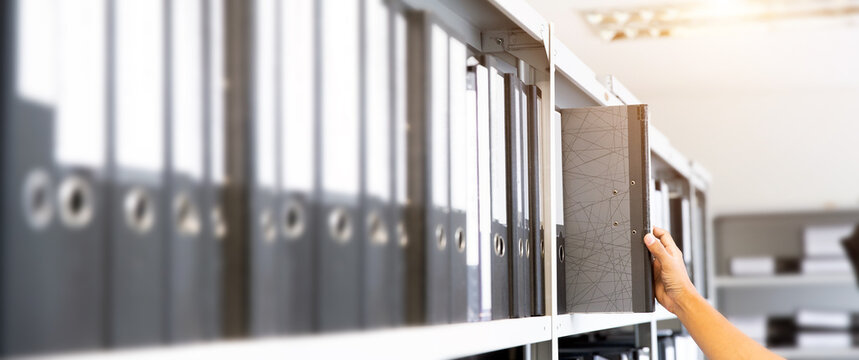 Hand of businessman office worker searching files and paperwork in the archive or document archiving storage room shelf for folder binder finding or data report record or workplace photo concept.