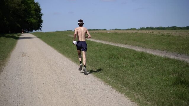 Running Man. A bare-chested man runs along a green meadow.