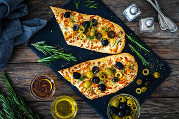 Focaccia alle olive - baked sandwich with green and black olives and rosemary on wooden background
