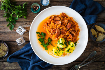Bigos - cooked cabbage with sliced sausage and boiled potatoes on wooden table