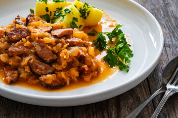 Bigos - cooked cabbage with sliced sausage and boiled potatoes on wooden table