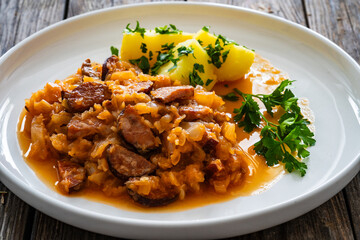 Bigos - cooked cabbage with sliced sausage and boiled potatoes on wooden table