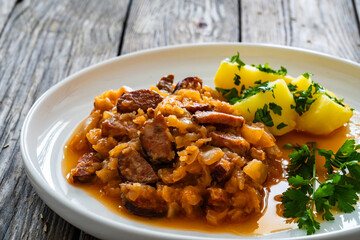 Bigos - cooked cabbage with sliced sausage and boiled potatoes on wooden table