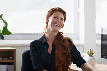 Businesswoman, laughing and office desk as entrepreneur at tech startup for small business,...