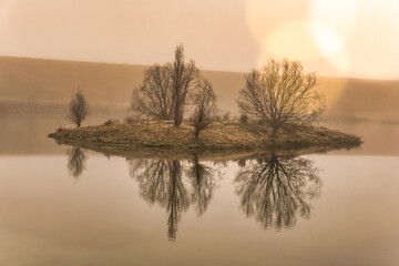 Island and tree silhouette reflected in the small loch  in early morning mist and fog