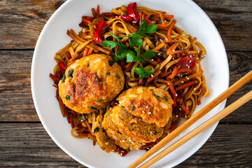 Asian style stir fried vegetables, pork meatballs and chow mein noodles on wooden table
