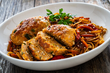 Asian style stir fried vegetables, pork meatballs and chow mein noodles on wooden table
