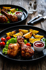 Oven baked chicken drumsticks with baked potato and fresh vegetables on wooden table
