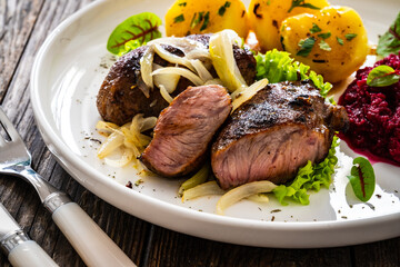 Baked pork cheeks with boiled potatoes and beetroots on wooden table
