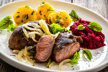 Baked pork cheeks with boiled potatoes and beetroots on wooden table
