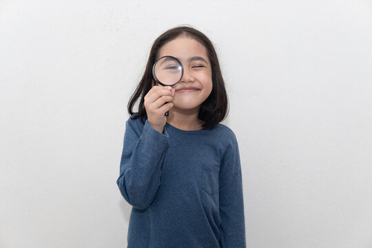Portrait of cute Asian Malay kid holding magnifying glass on white background.