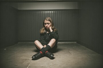 A scared and battered woman sitting alone in a dark and oppressive room in despair