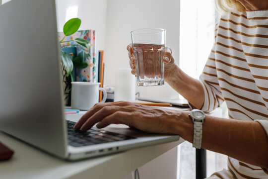 A senior woman by the computer with a glass of water