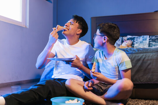 Two friends at home watching movies and eating junk food.